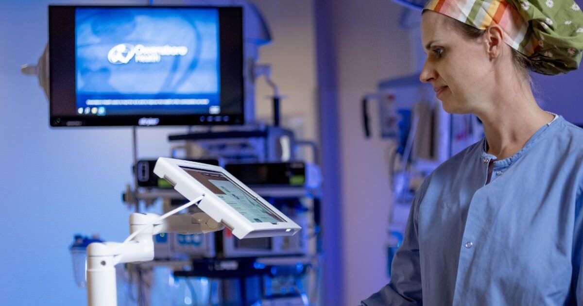 A person stands at a tablet stand in an operating room.