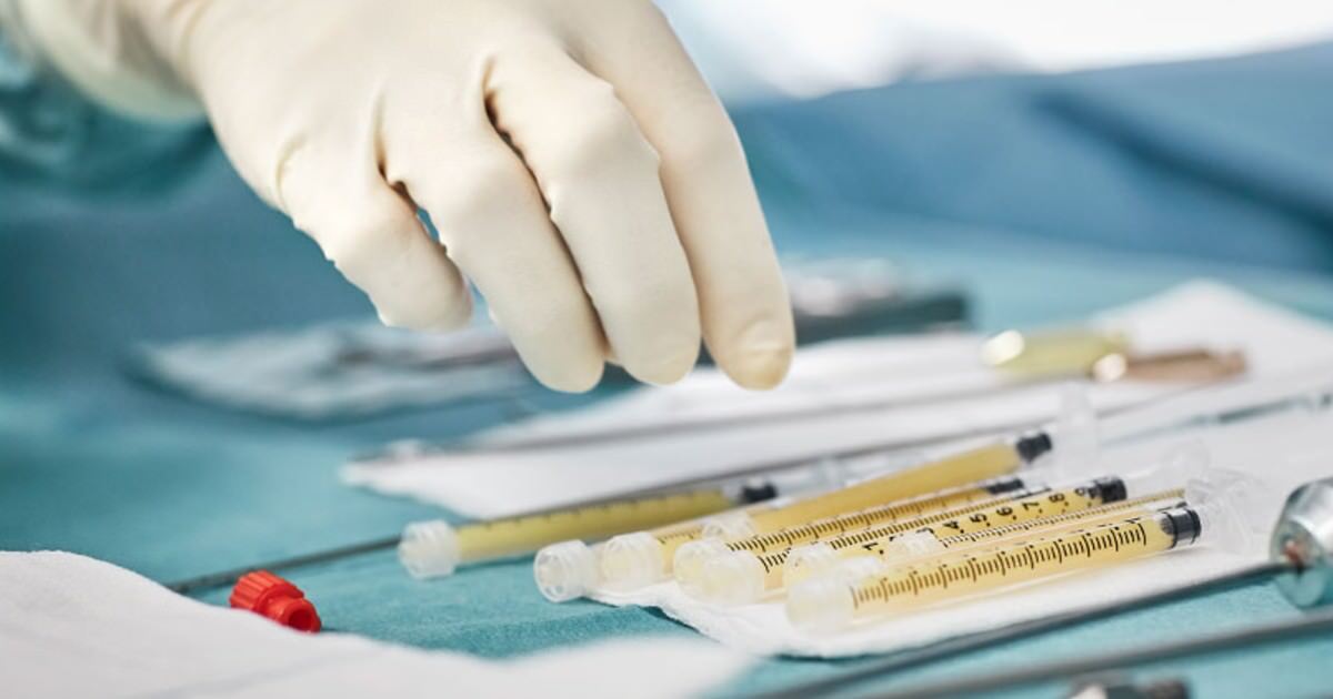Tray of surgical supplies with a gloved hand reaching to select an item