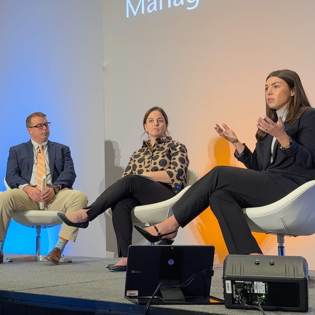 Three panelists seated on stage during a session at the ORBM 2026 conference, Amy Brown speaking